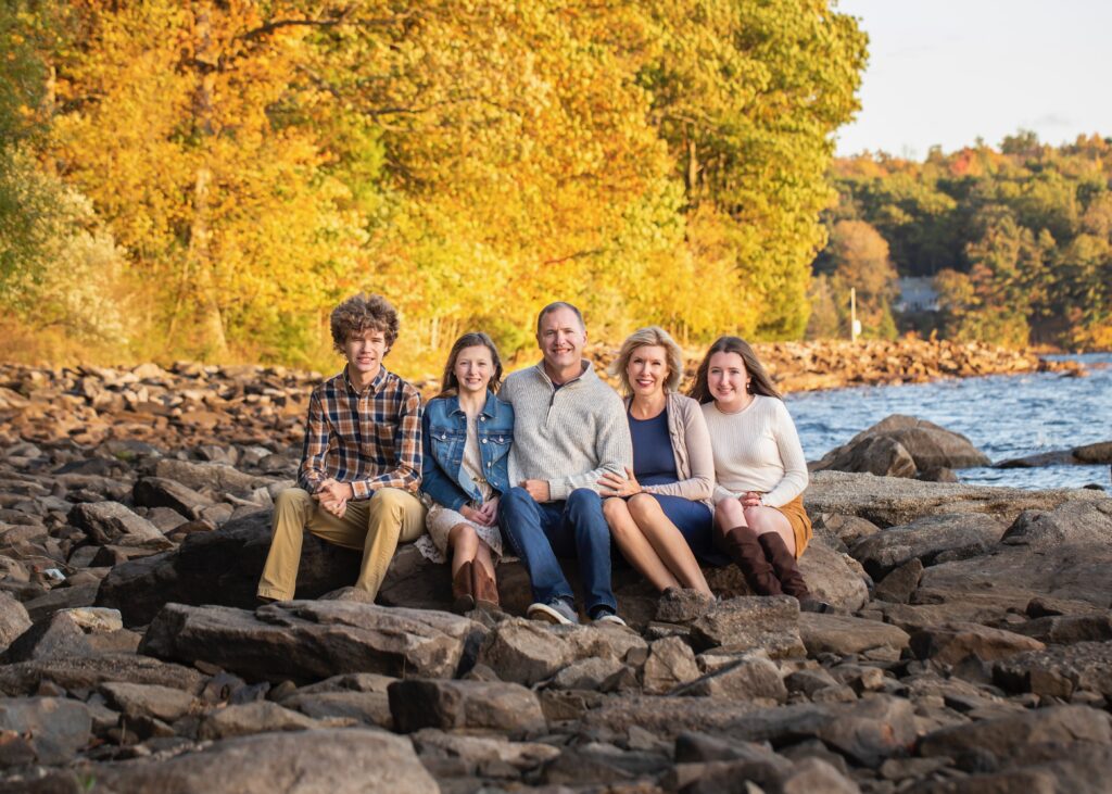 family sitting on deep creek lake rocks with fall trees in background