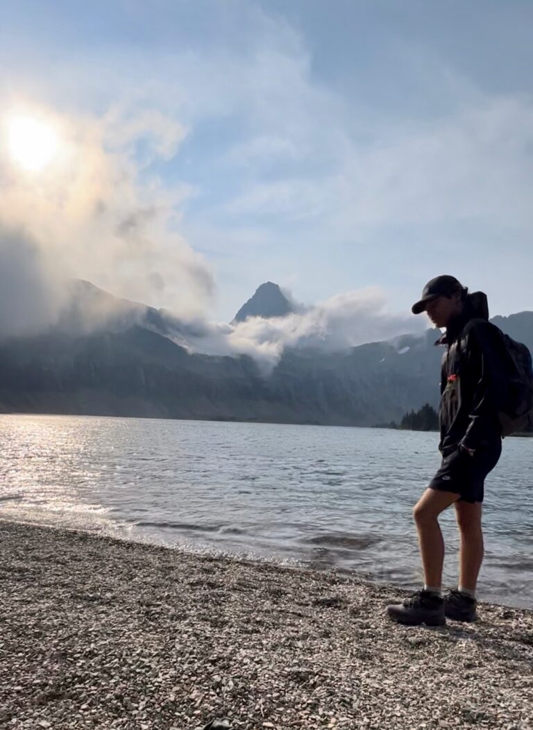 Man standing at Hidden Lake with clouds surrounding mountains in the background.